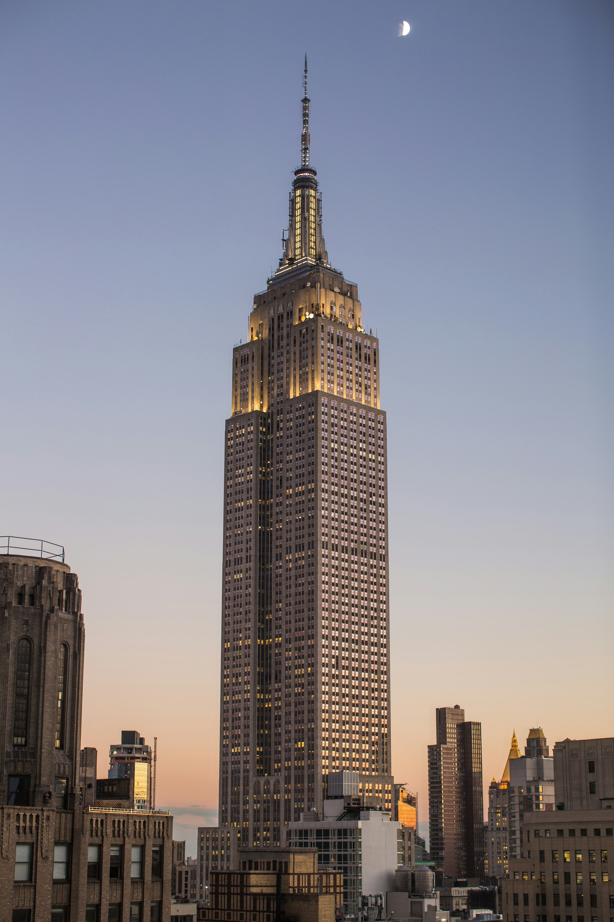 Generate an image of: Extreme low angle looking up at a dark metallic building facade with perfect symmetry, moody sky, glowing yellow accents on the steel
